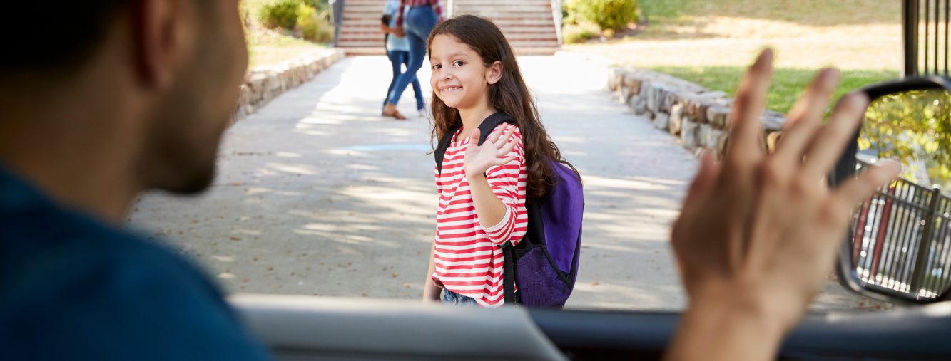 Smiling elementary-aged girl with purple backpack waving during school drop-off as a parent waves from a car window