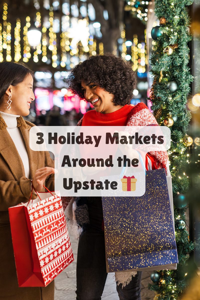 Two women smiling and carrying holiday shopping bags at a festive outdoor market in Upstate South Carolina.